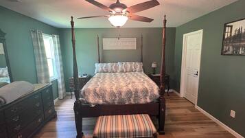 A bedroom with a four-poster bed, a nightstand, a bench, a dresser, and a ceiling fan.