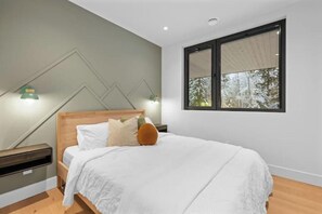 A bedroom with a bed, a nightstand, a lamp, and a window with a view of trees. - Luxury Riverside Retreat near Whistler (Whistler)