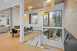 A modern interior with a staircase, dining area, and large windows with snowy views. - Luxury Riverside Retreat near Whistler (Whistler)