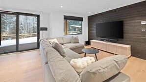 Un salon moderne doté d’un grand téléviseur à écran plat, d’un canapé d’angle et d’un meuble de rangement en bois pour les appareils multimédias.