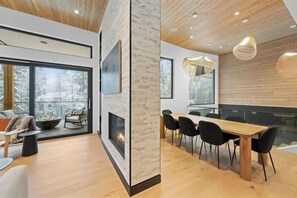 A modern interior with a fireplace, dining area, and large windows. - Luxury Riverside Retreat near Whistler (Whistler)