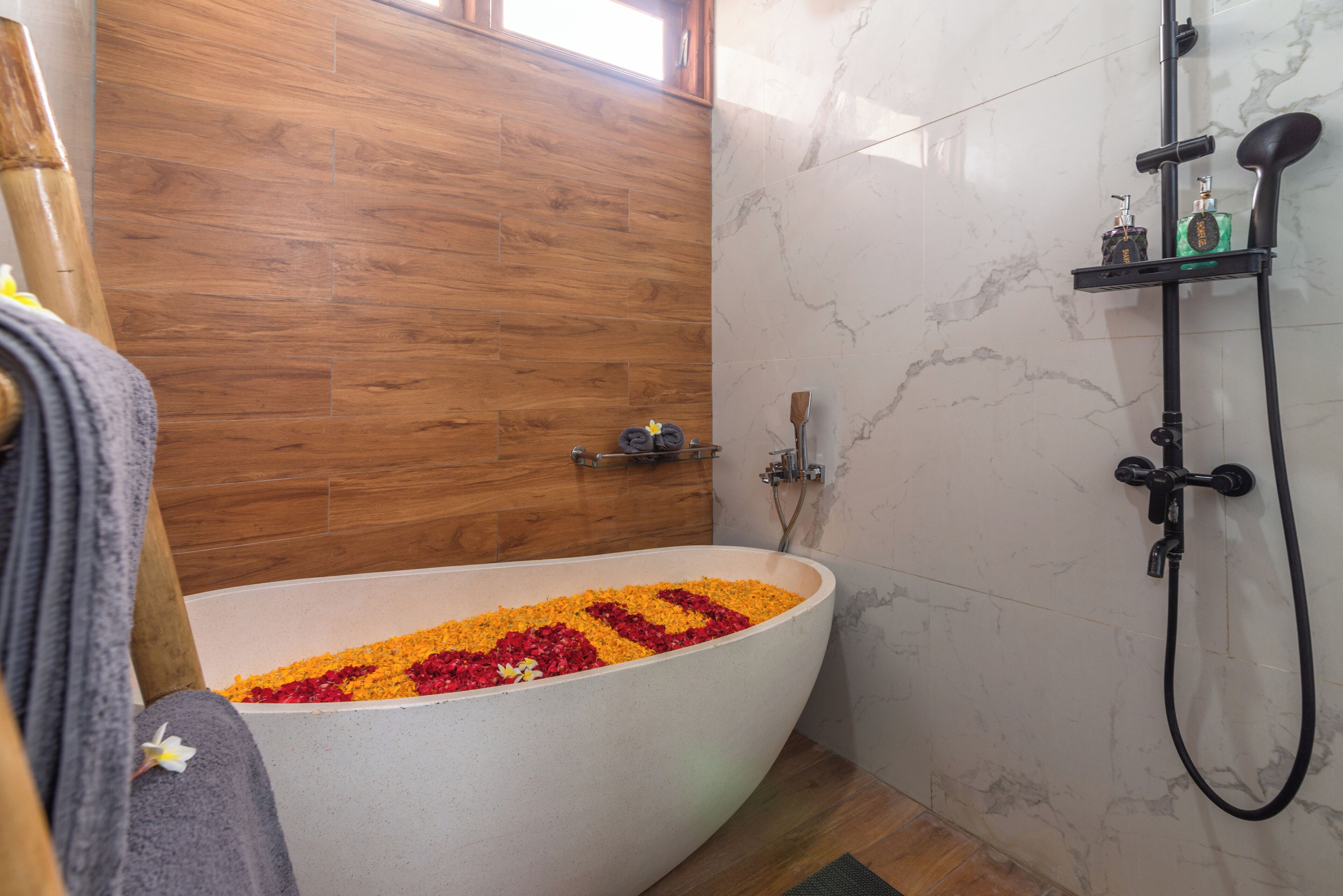 Une salle de bain avec une baignoire îlot remplie de pétales de fleurs, un plancher en bois et un mur en marbre.