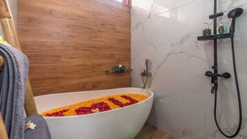 Une salle de bain avec une baignoire îlot remplie de pétales de fleurs, un plancher en bois et un mur en marbre.