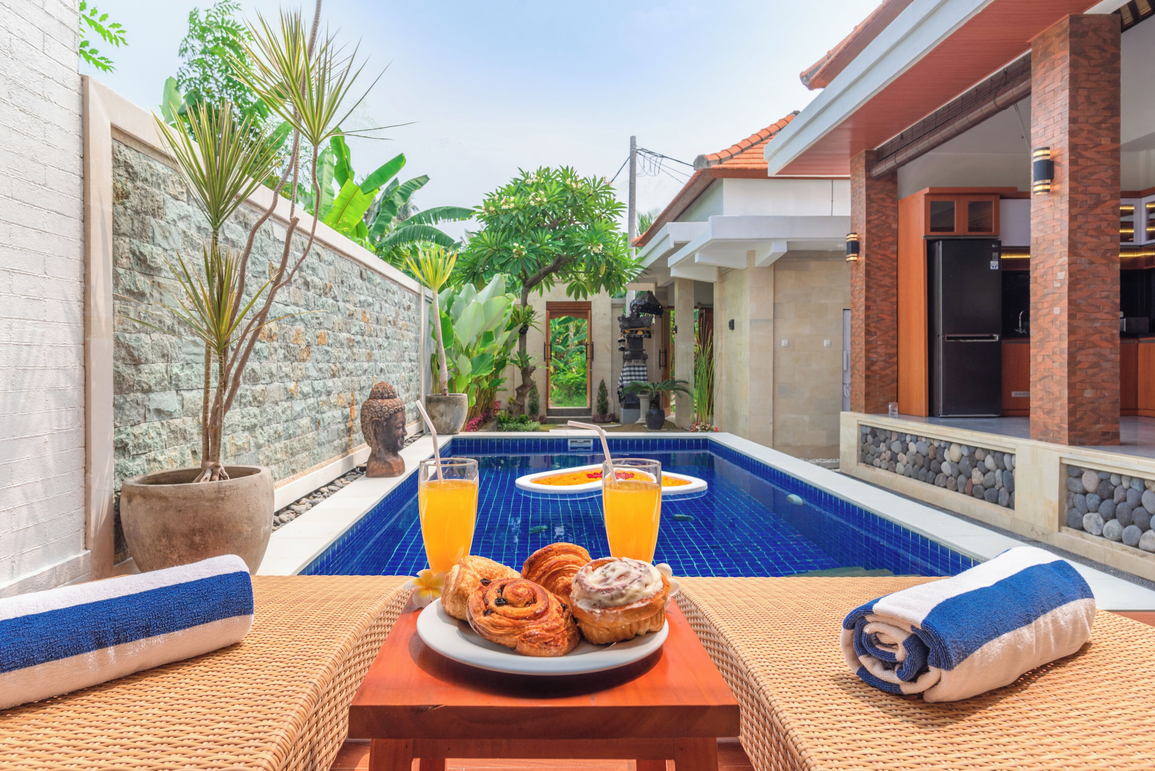 Un cadre agréable au bord de la piscine, avec une table dressée pour le petit-déjeuner, comprenant des viennoiseries et des boissons.