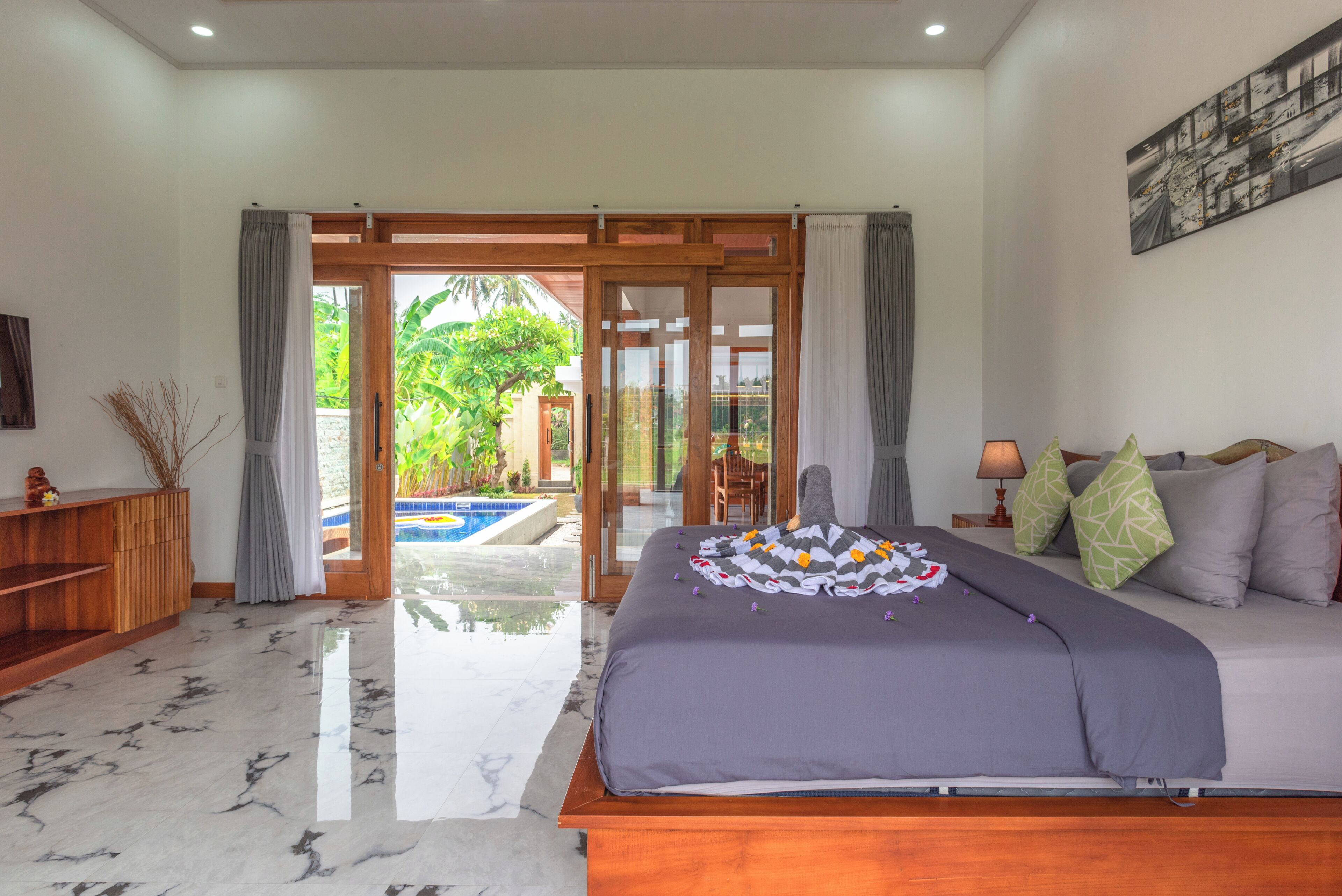A bedroom with a bed, a nightstand, a lamp, and a view of a swimming pool.