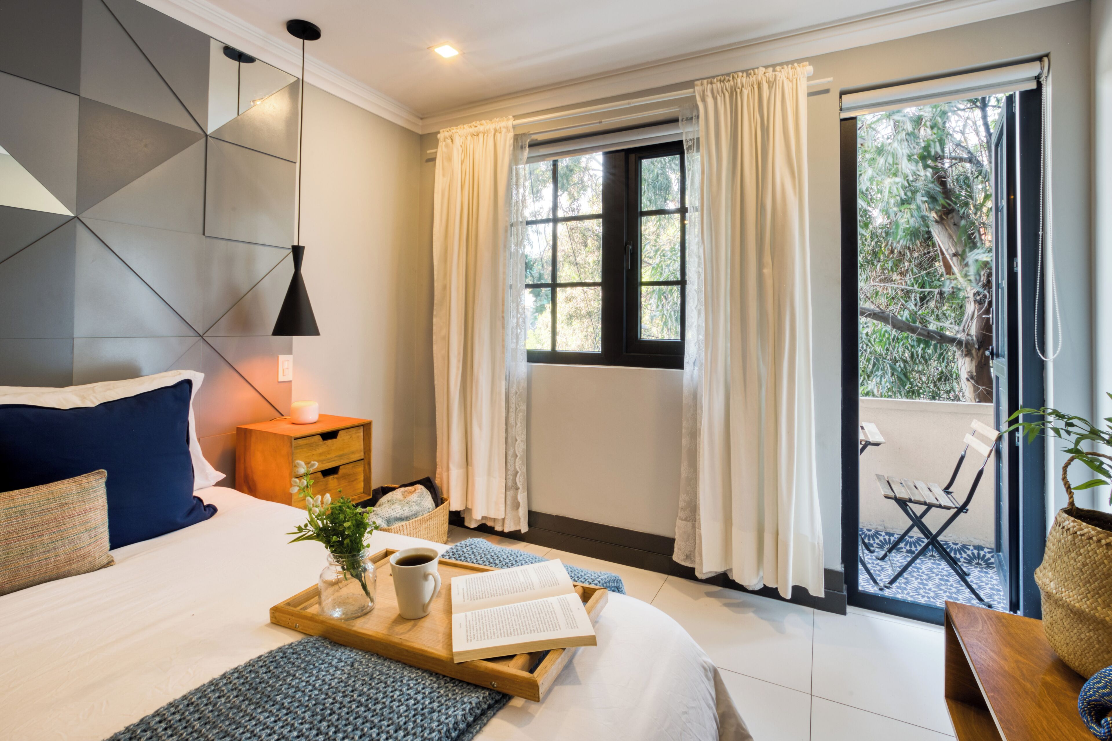 A modern bedroom with a bed, bedside table, reading materials, and a view of the outdoors.