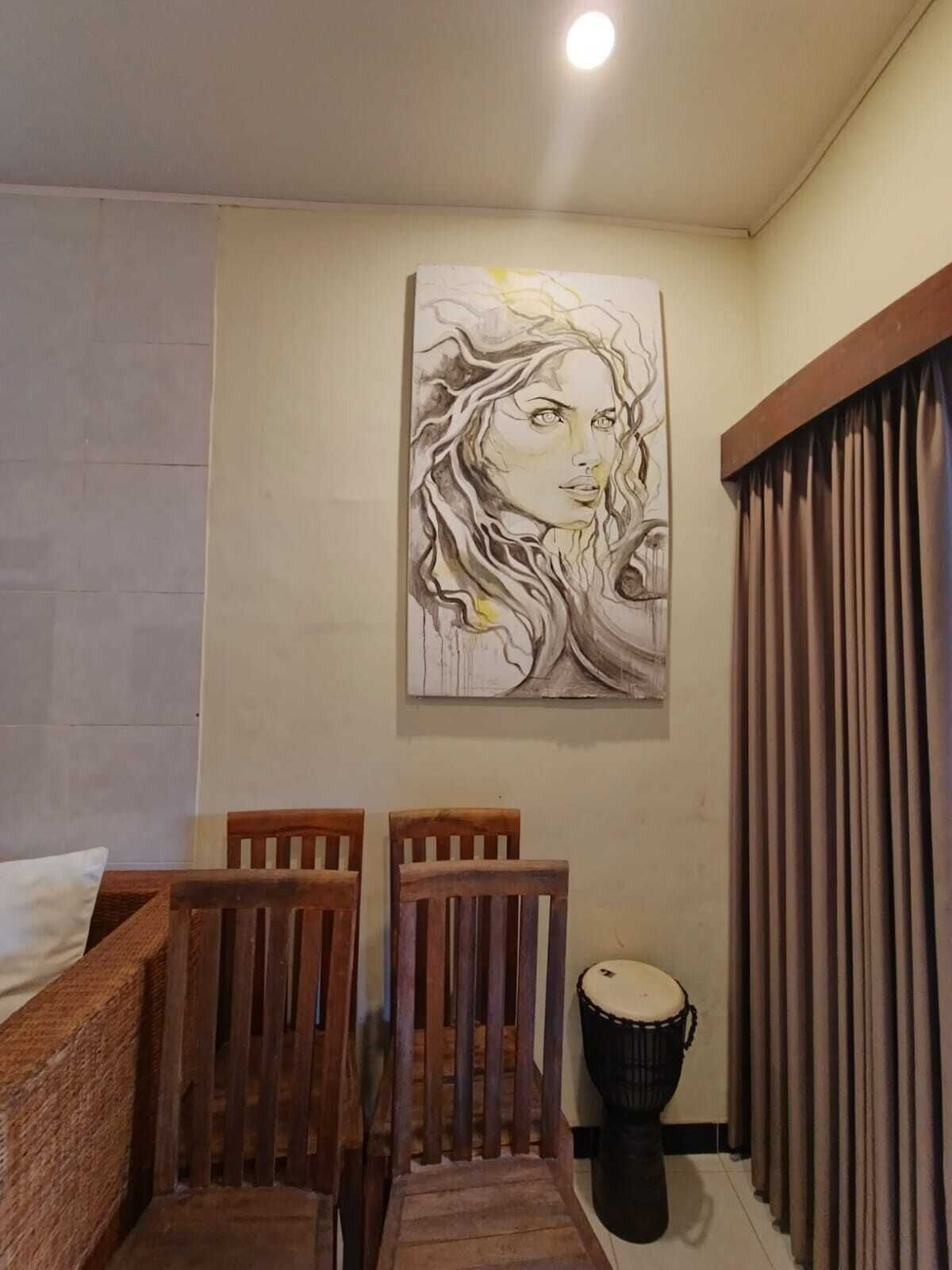 A room with a wooden chair, a drum, and a painting on the wall.