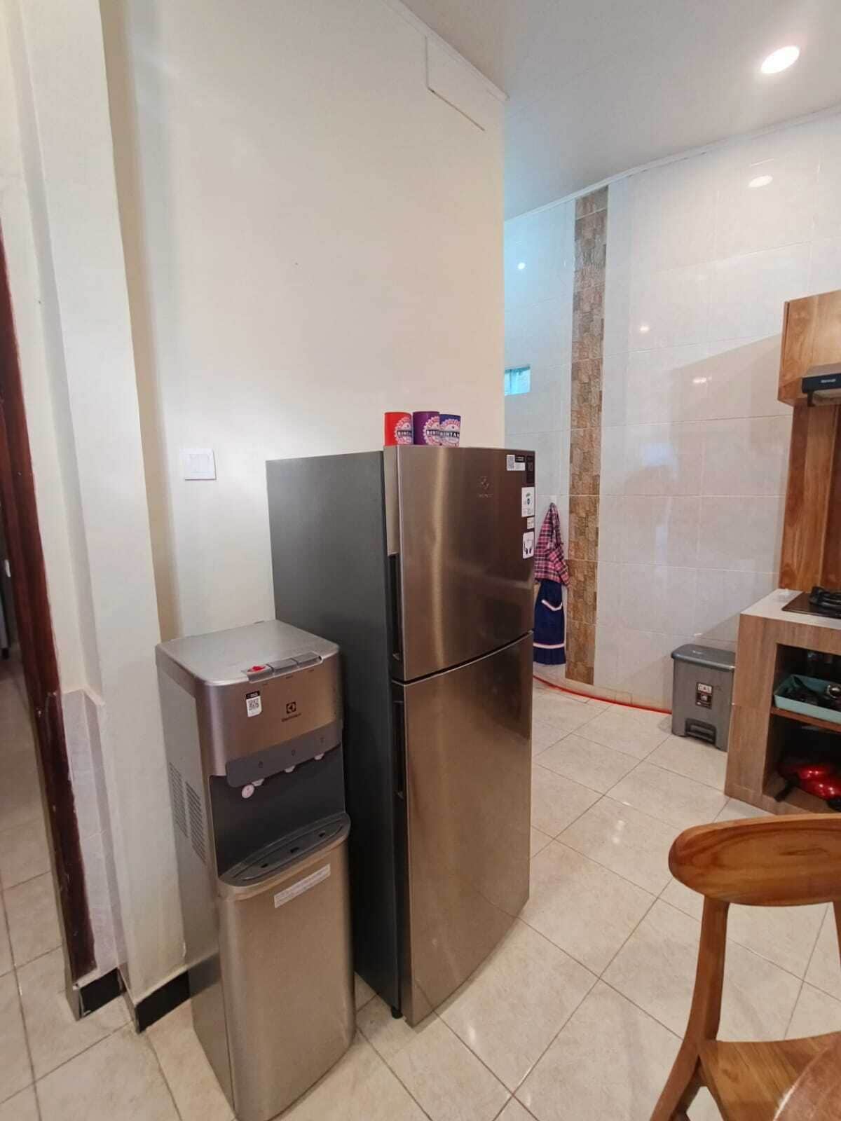 Cocina compacta con refrigerador de acero inoxidable, dispensador de agua y un pequeño cubo de basura.