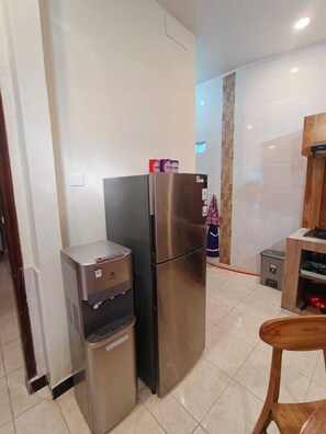 Cocina compacta con refrigerador de acero inoxidable, dispensador de agua y un pequeño cubo de basura.