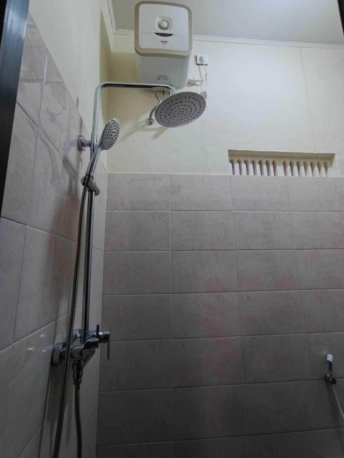A shower area with a handheld showerhead and a wall-mounted showerhead, both with hoses.