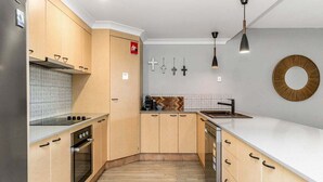 Een moderne keuken met houten kastjes, een inbouwoven, een wit aanrechtblad en een hangende hanglamp.