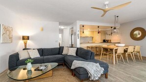Een moderne woonkamer met een modulaire bank, een glazen salontafel en een eethoek met houten stoelen en een tafel.