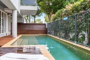 A swimming pool with a wooden deck area, surrounded by a metal fence and trees. - Indiah - Unit 3, Byron Quarter Apartments (Byron)
