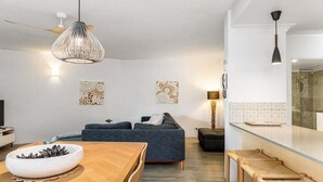 Een moderne woonkamer met een donkere bank, een houten eettafel en een hangende lamp.