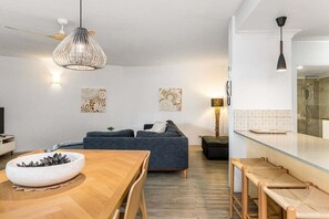 A modern living room with a dark sofa, a wooden dining table, and a hanging light fixture. - Indiah - Unit 3, Byron Quarter Apartments (Byron)
