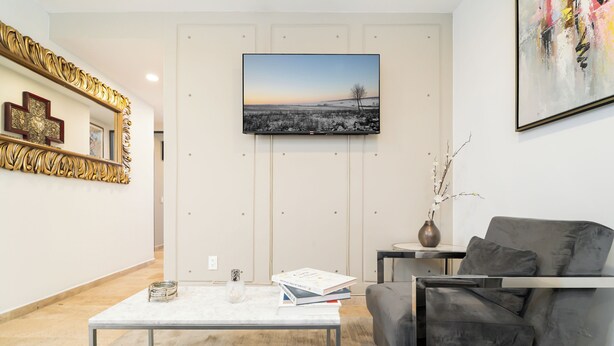A modern living room with a flat-screen TV mounted on the wall, a coffee table, a grey sofa, and a decorative mirror with a golden frame. - Napoles Elegance · A pasos de WTC (Ciudad de México)