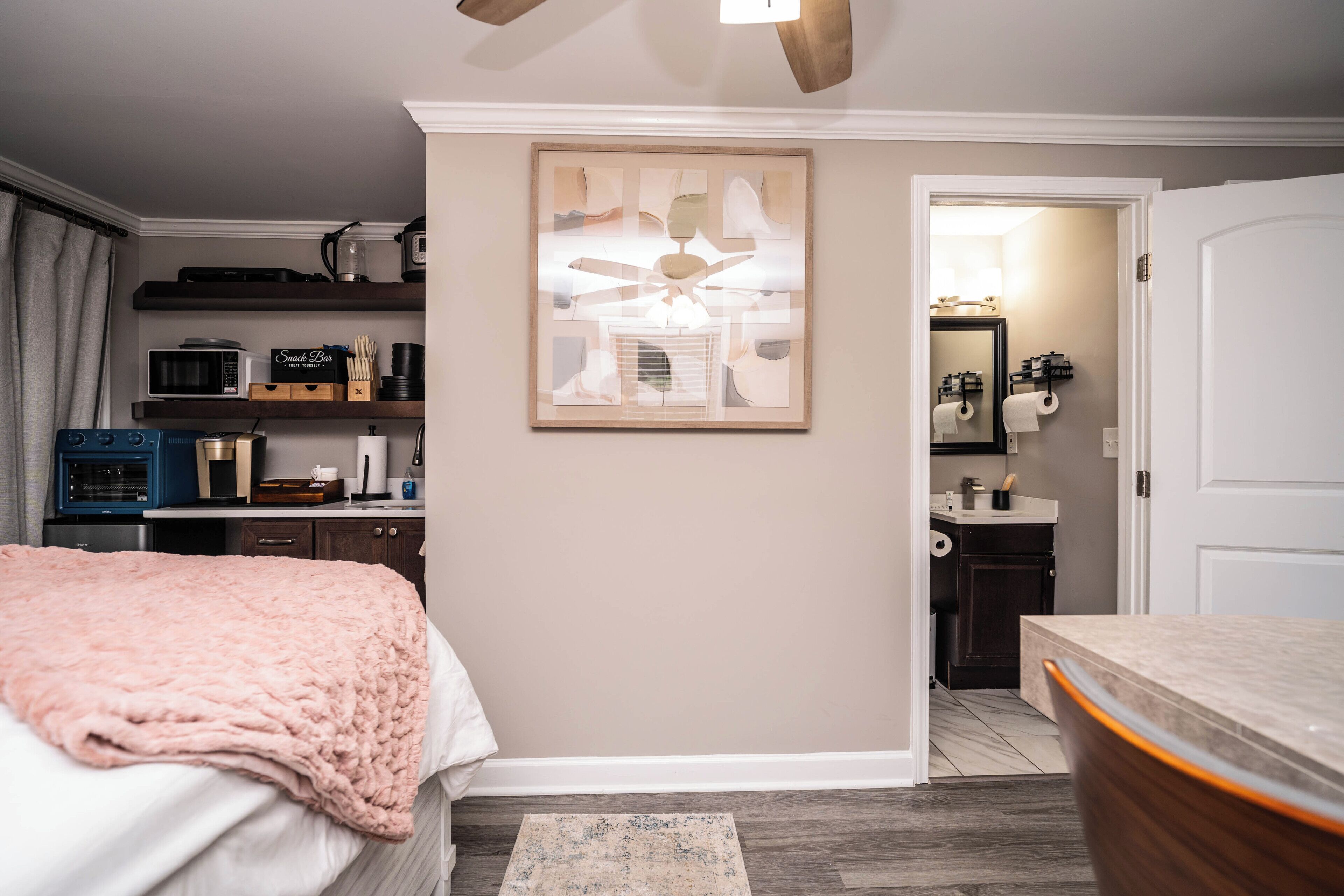 A bedroom with a bed, a bedside table, a dresser, a microwave, a coffee maker, and a ceiling fan.