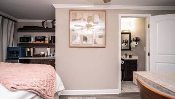 A bedroom with a bed, a bedside table, a dresser, a microwave, a coffee maker, and a ceiling fan.
