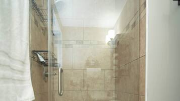 A walk-in shower with a glass door, beige tiles, and a white bathtub.