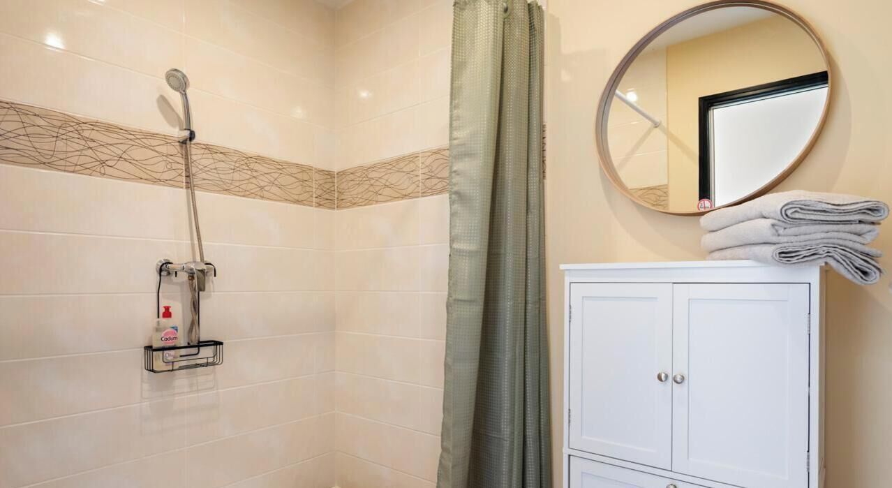 A bathroom with a shower, a mirror, and a cabinet.
