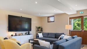 Ein Wohnzimmer mit Flachbildfernseher, Sofa, Sesseln und einem kleinen Tisch.