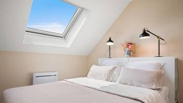 Una camera da letto con un lucernario, un letto con lenzuola bianche, due lampade da comodino e un piccolo vaso con fiori sul tavolino.