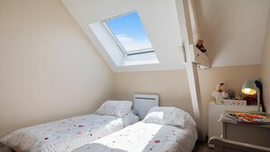 Ein Schlafzimmer mit zwei Betten, einem Oberlicht, einem Nachttisch mit Lampe und einer kleinen Ablage mit Spielzeug.