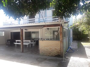 A covered outdoor area with a table and chairs, a brick wall, and a window overlooking a residential building. - Two-story house with pool and small soccer field in Itapoá-SC (Itapoá)
