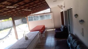 Een overdekt terras met een tafel, bankjes en een loungebank.