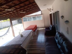A covered outdoor seating area with a table, benches, and a sofa. - Two-story house with pool and small soccer field in Itapoá-SC (Itapoá)