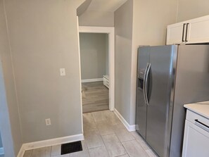 A kitchen with a stainless steel refrigerator, white cabinets, and a wooden floor.