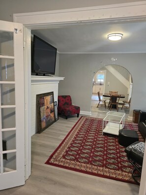 A living room with a fireplace, a television, a red floral chair, a patterned rug, and a staircase leading to another room.
