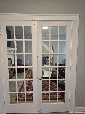 En vit dörr med glaspaneler som leder in till ett rum med en trappa, en stol och en mönstrad matta.