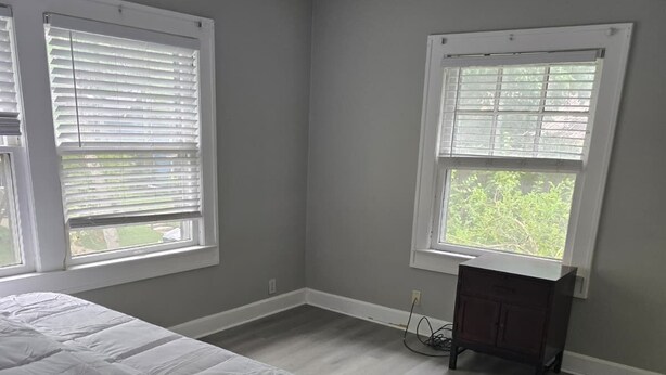 A bedroom with a bed, a dresser, and two windows with blinds.