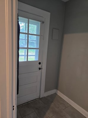 A white door with a glass panel, a doorknob, and a small light switch on the wall.