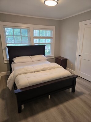 A bedroom with a bed, two windows, a door, and a nightstand.