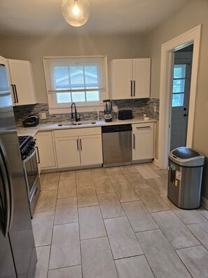 A kitchen with white cabinets, a stainless steel dishwasher, a black toaster, and a trash can.