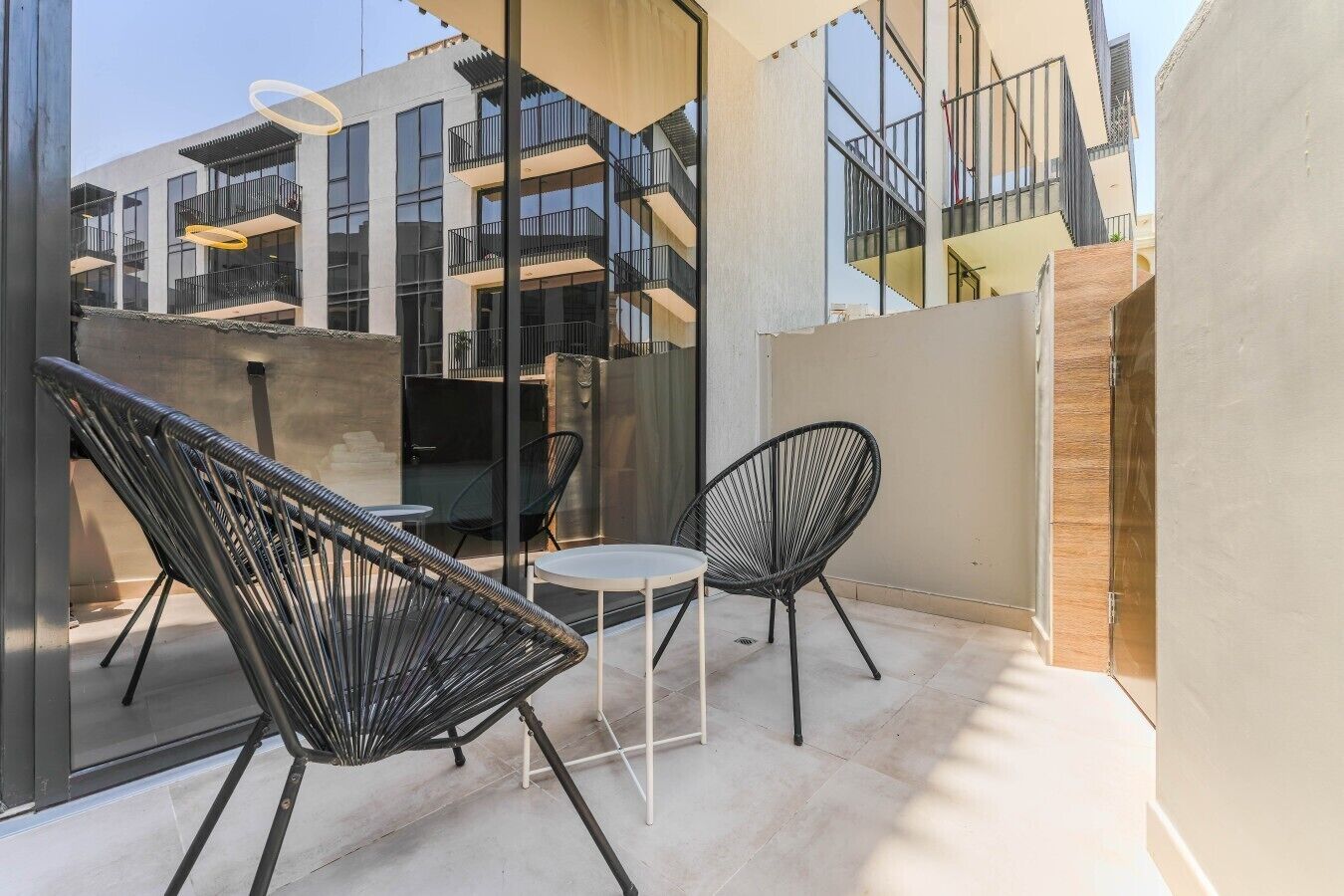 A modern outdoor seating area with two black chairs and a small table, overlooking a building with balconies and a staircase.