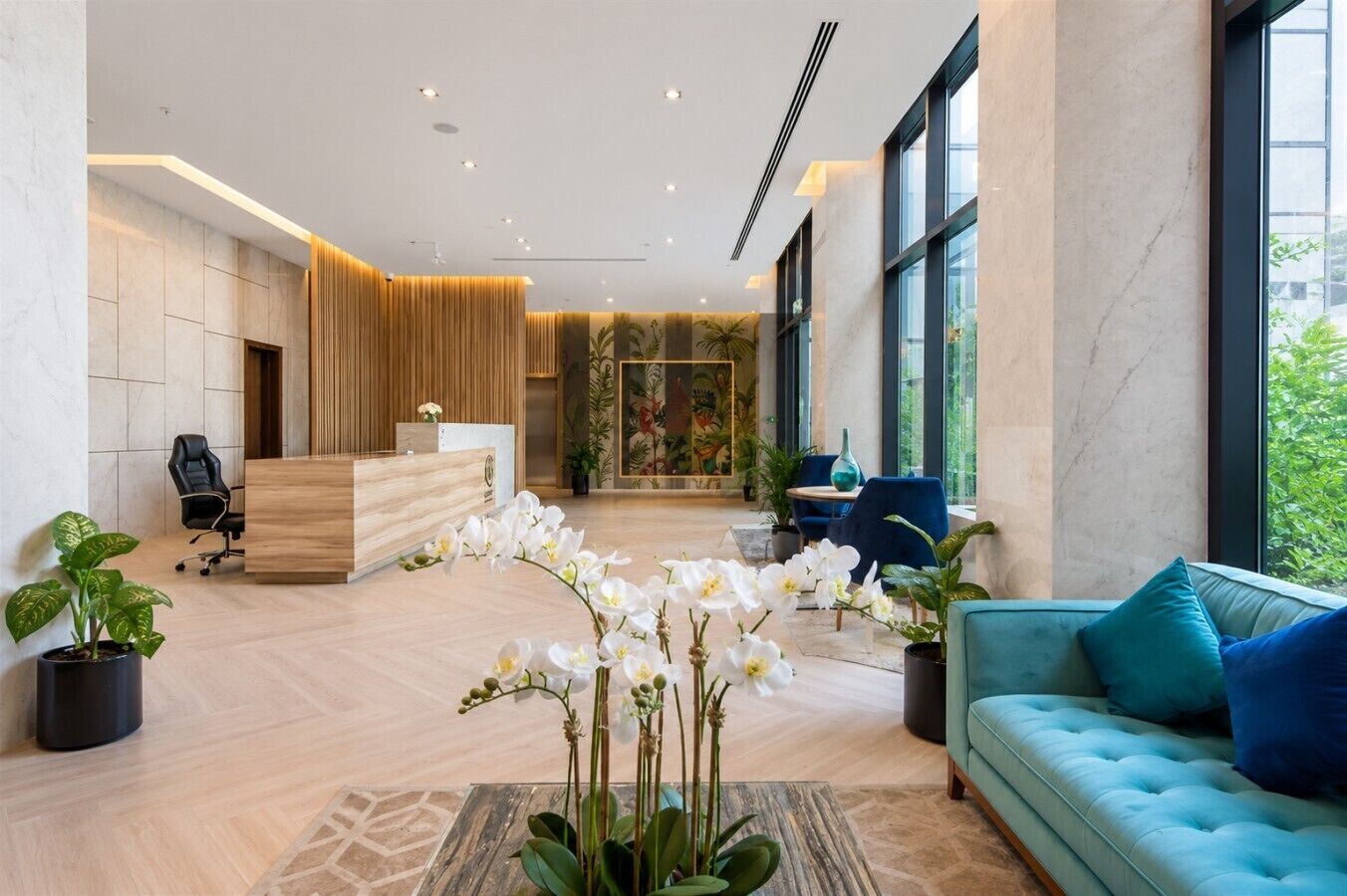 A modern reception area with a wooden desk, a blue sofa, and potted plants.