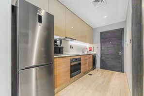 A modern kitchen with stainless steel appliances, wooden cabinets, and a built-in oven. - HAVN - Studio in Q Gardens Boutique, Arjan (Dubai)