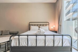 A neatly made bed with white linens, a metal headboard, and a bedside table with two lamps. - HAVN - Studio in Q Gardens Boutique, Arjan (Dubai)