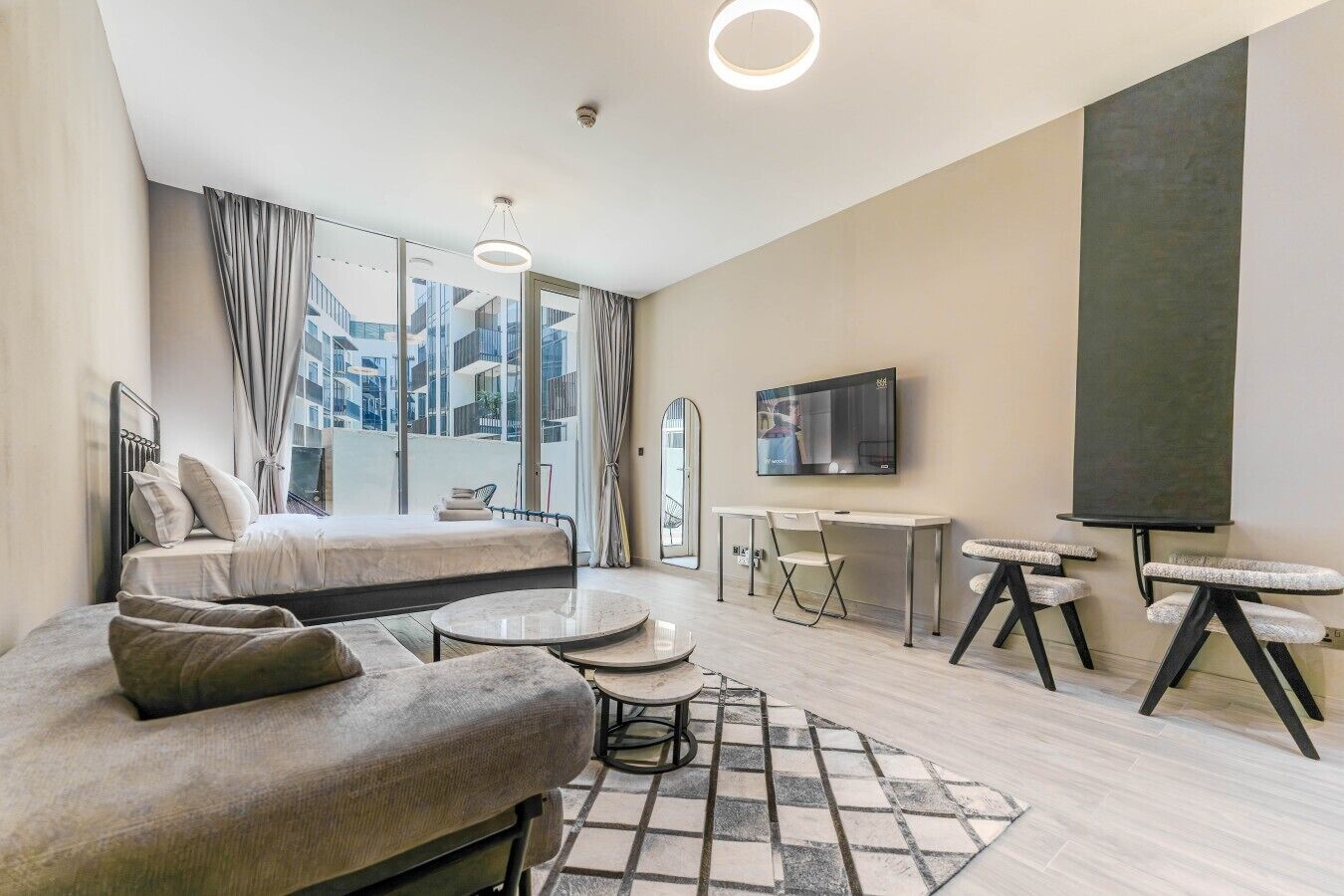 Ein modernes Hotelzimmer mit Bett, einer Couch, einem Schreibtisch, einem Fernseher und einem Balkon mit Vorhängen.