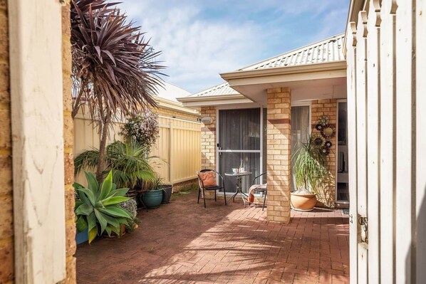 A patio area with a brick floor, a table with chairs, and various potted plants. - Station Road Retreat (Margaret River)