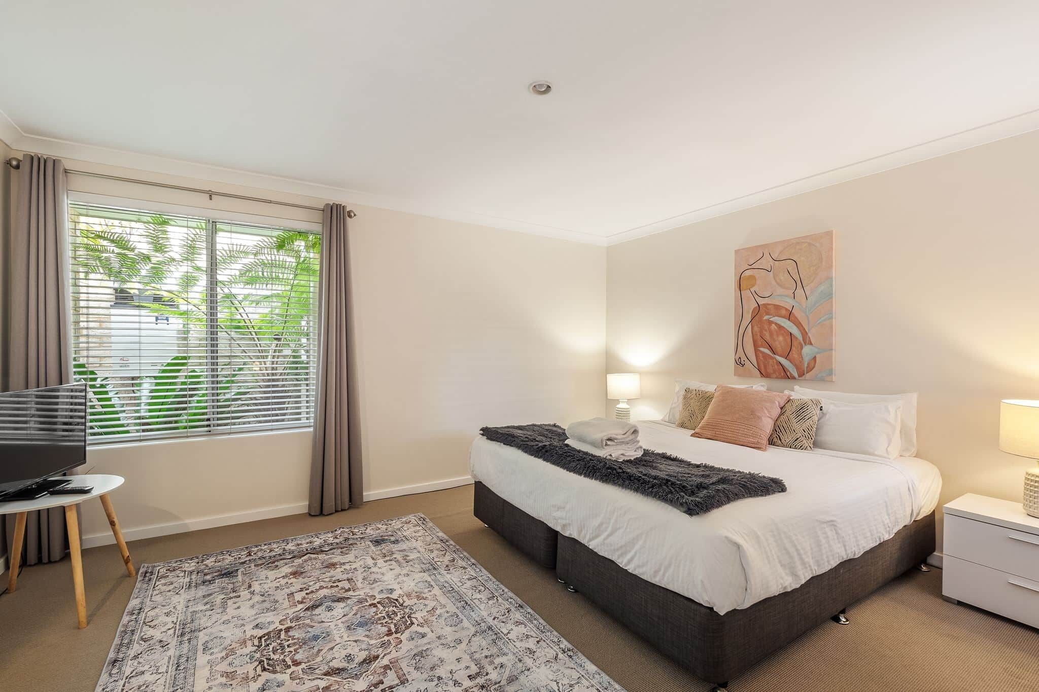 A bedroom with a bed, bedside tables, a TV, and a window with curtains.