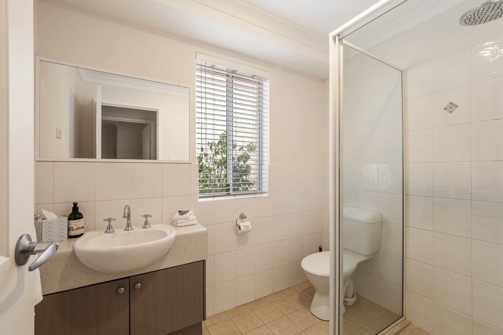 A bathroom with a sink, mirror, toilet, and shower.