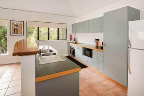 A modern kitchen with a central island, a sink, and a refrigerator. - Gas Bay Beach House Margaret River (Gnarabup)