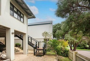 A modern building with a staircase leading to a covered entrance, surrounded by greenery and a paved area. - Gas Bay Beach House Margaret River (Gnarabup)