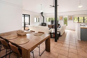 A modern living space with a dining table, chairs, a sofa, and a kitchen area. - Gas Bay Beach House Margaret River (Gnarabup)