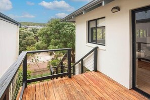 Eine Holzterrasse mit schwarzer Geländer, einer weißen Außenwand und Blick auf Grünflächen und Hügel im Hintergrund.