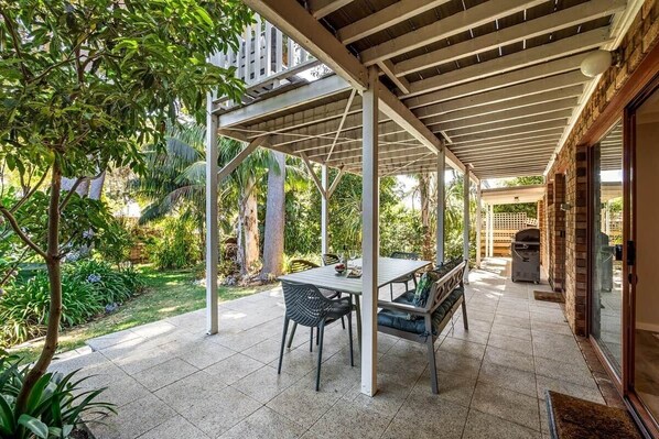 Eine Terrassengruppe mit Tisch und Stühlen, umgeben von Grünflächen und einem Grillplatz mit Backsteinelementen.